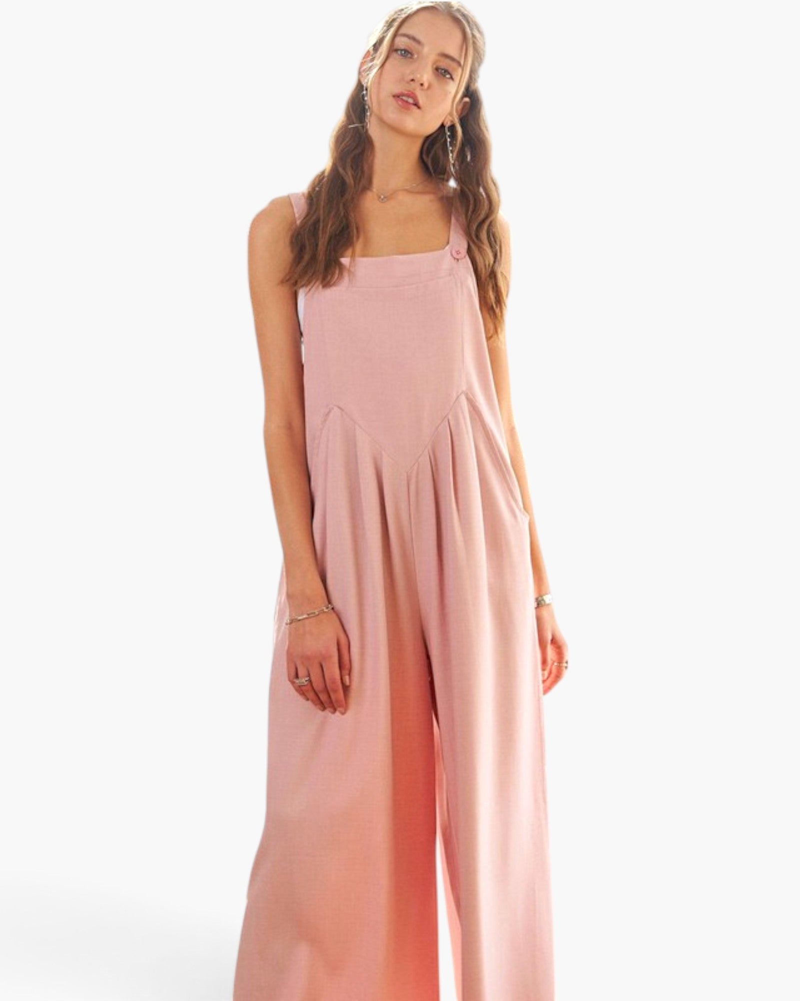 A woman modeling a light pink sleeveless wide-leg jumpsuit against a plain white studio background.