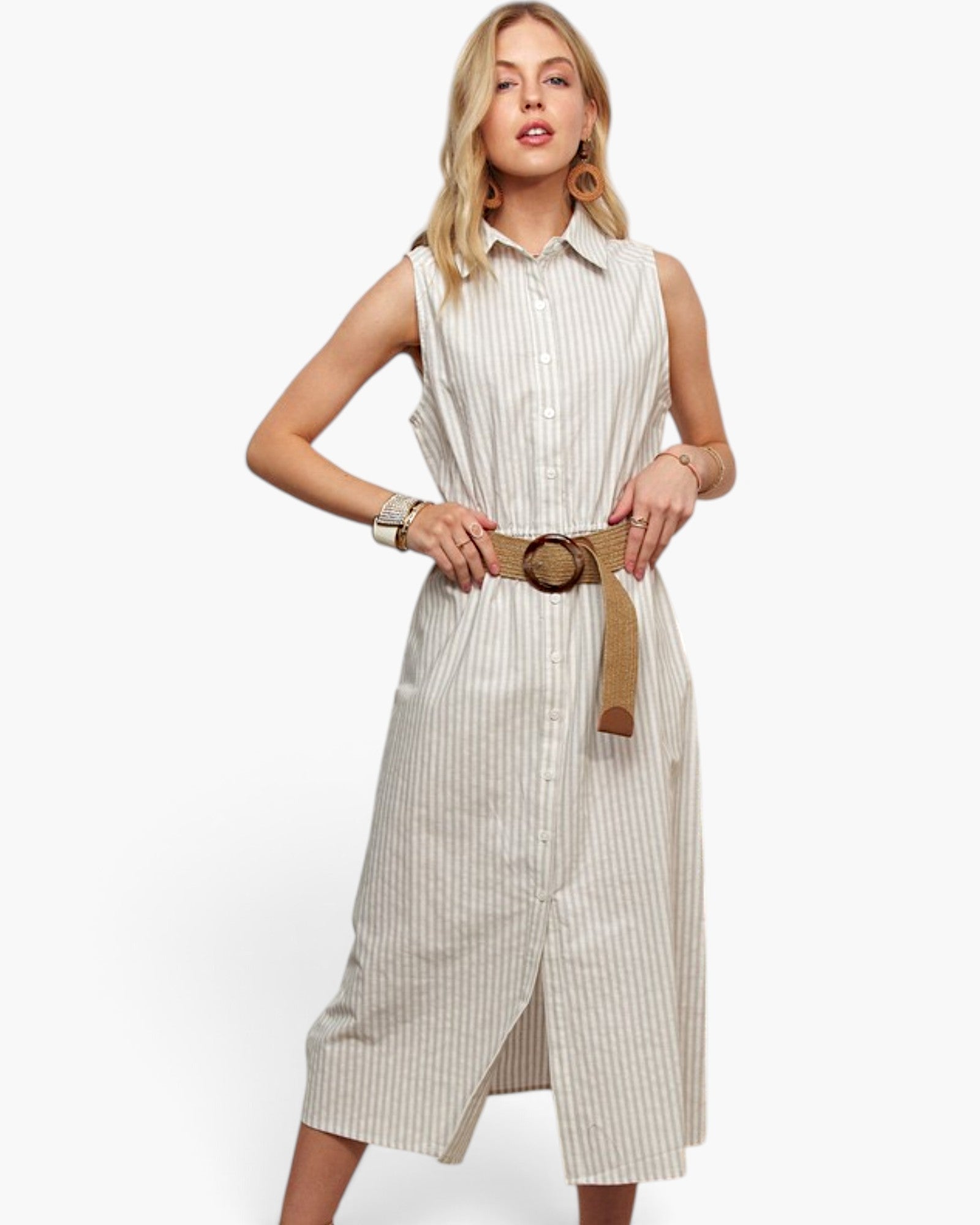A woman modeling a sleeveless, button-front midi dress with thin vertical pinstripes in a light beige and white colorway, styled with a wide tan belt featuring a large round brown buckle, against a plain white studio background.