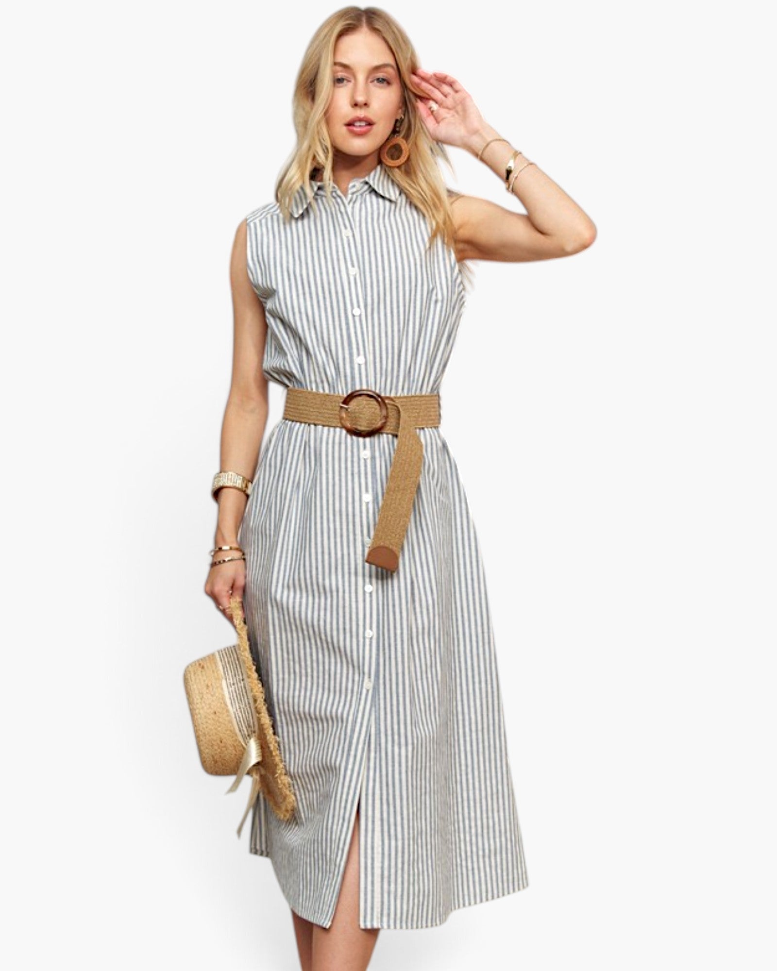 A woman models a sleeveless, button-front midi dress with vertical gray and white stripes, styled with a tan belt and holding a straw hat against a plain white background.