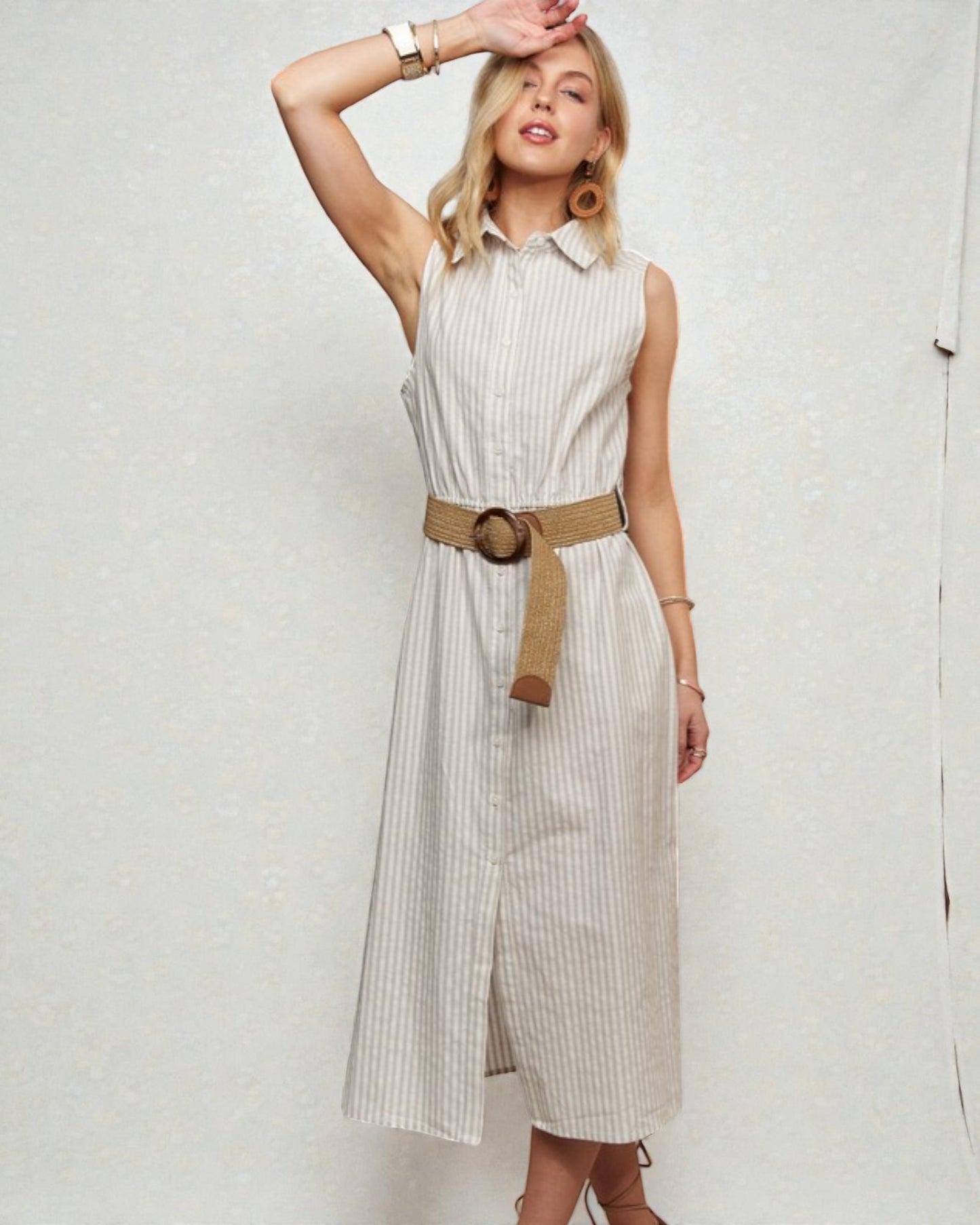 Woman wearing a beige sleeveless dress with a belt against a white background