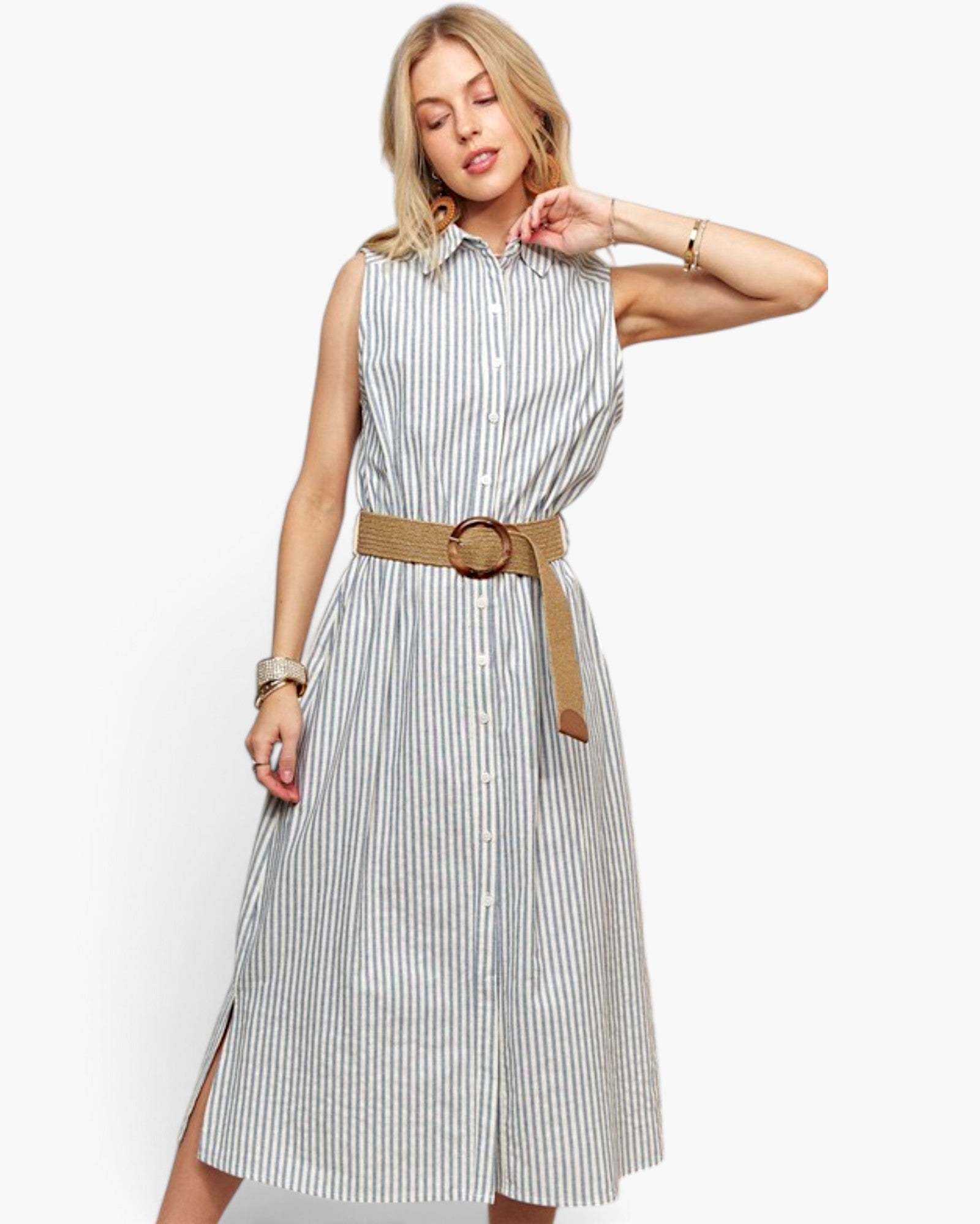A woman modeling a sleeveless midi shirt dress with vertical blue and white stripes, featuring a button-down front, collar, and a tan woven belt with a large round buckle.