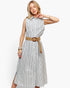 A woman modeling a sleeveless midi shirt dress with vertical blue and white stripes, featuring a button-down front, collar, and a tan woven belt with a large round buckle.