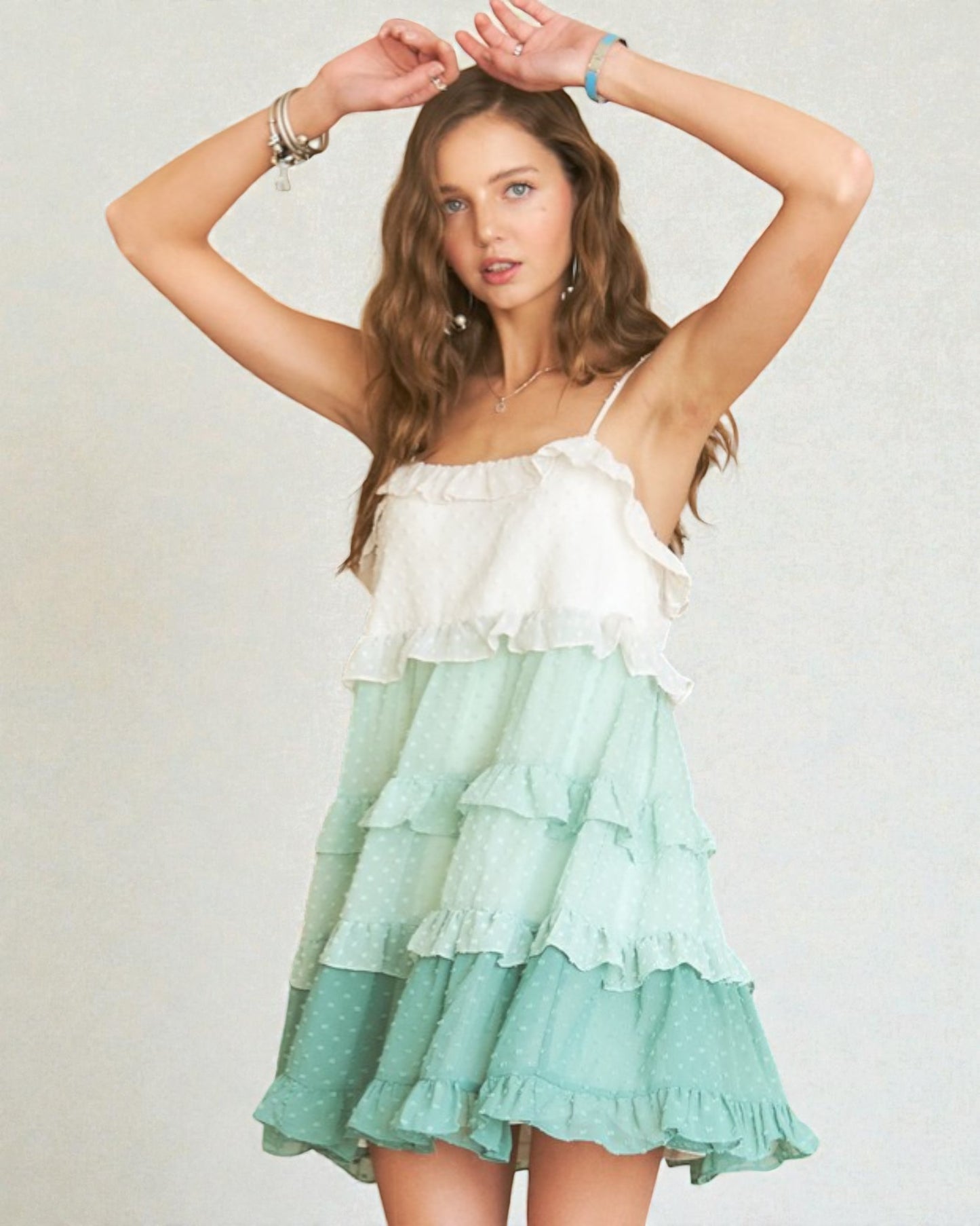 Woman wearing a white and green tiered dress against a plain background