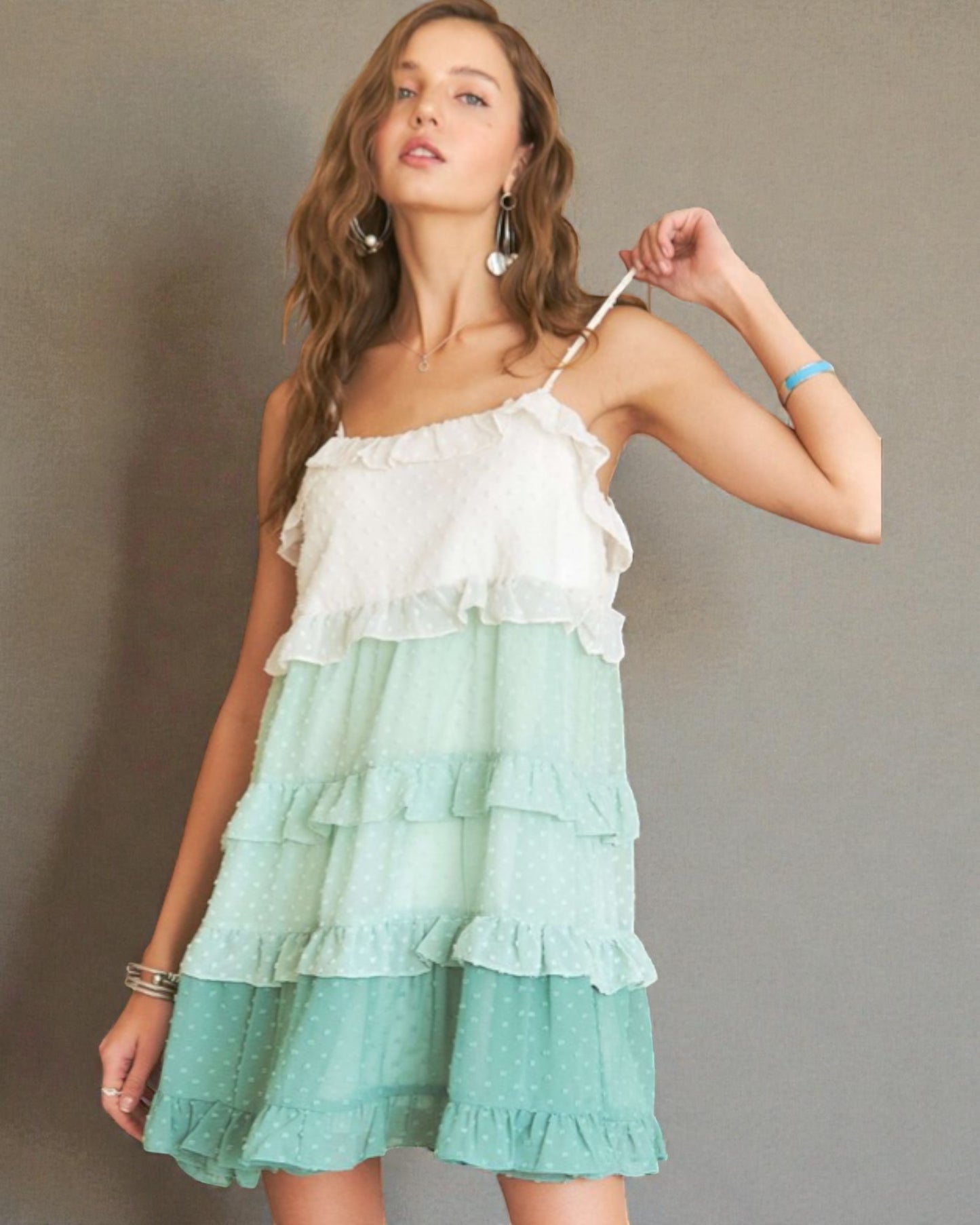 Woman wearing a white and green tiered dress against a plain background