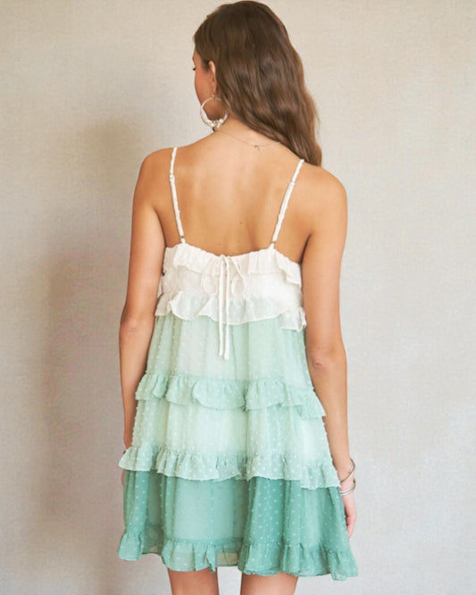 Woman wearing a white and green tiered dress against a plain background