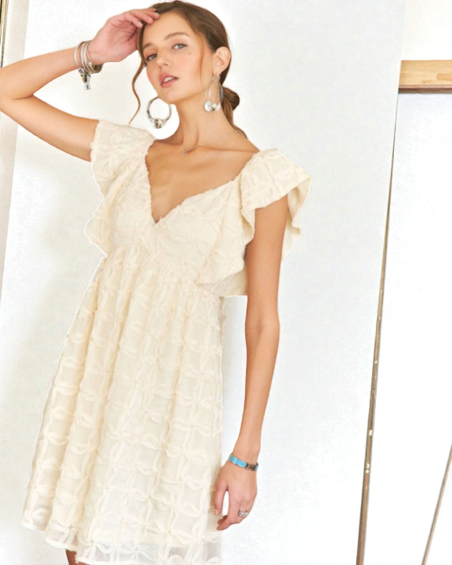 Woman wearing a beige dress with ruffled sleeves against a white background