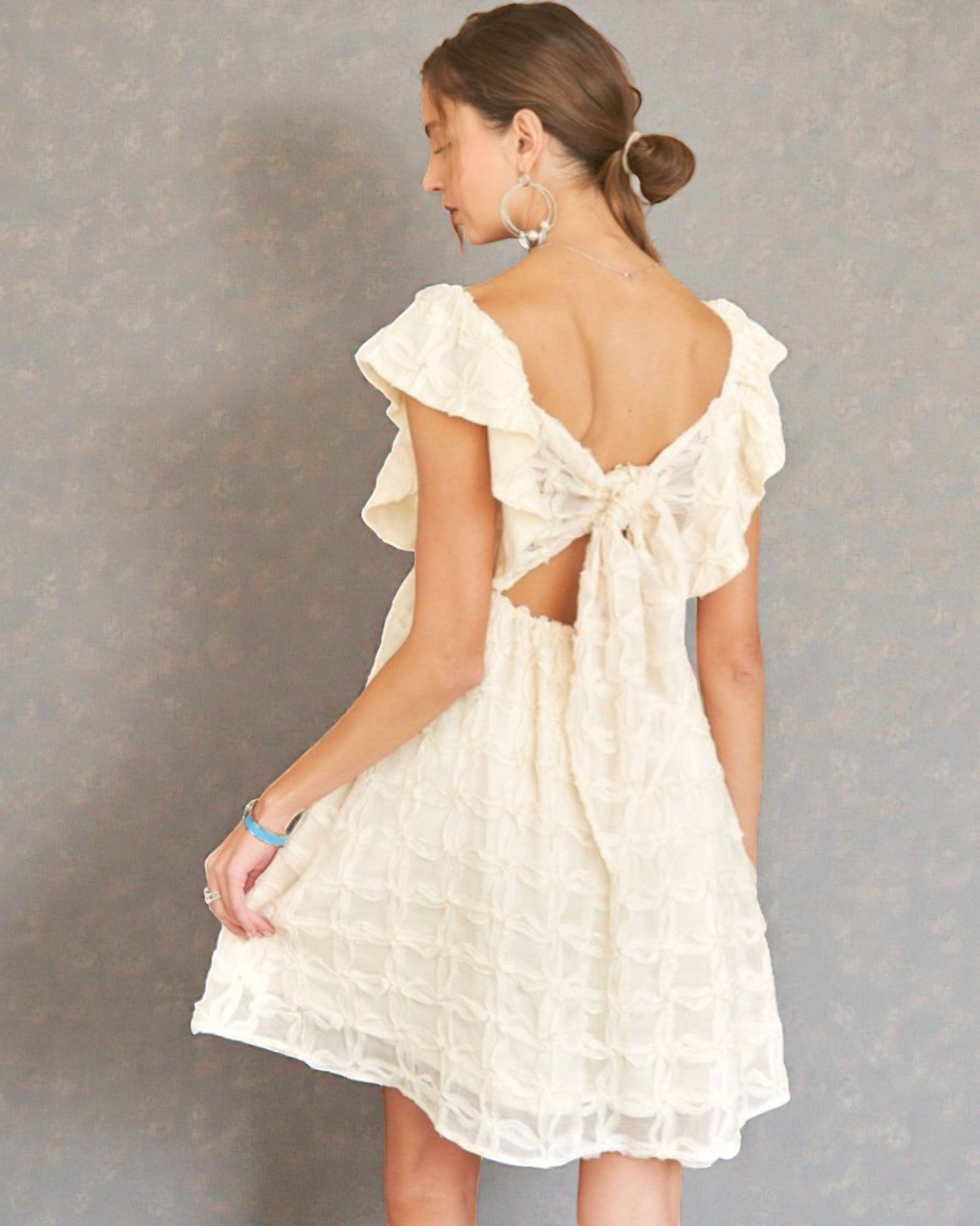 Woman wearing a white dress with ruffled sleeves and cut-out back against a gray background