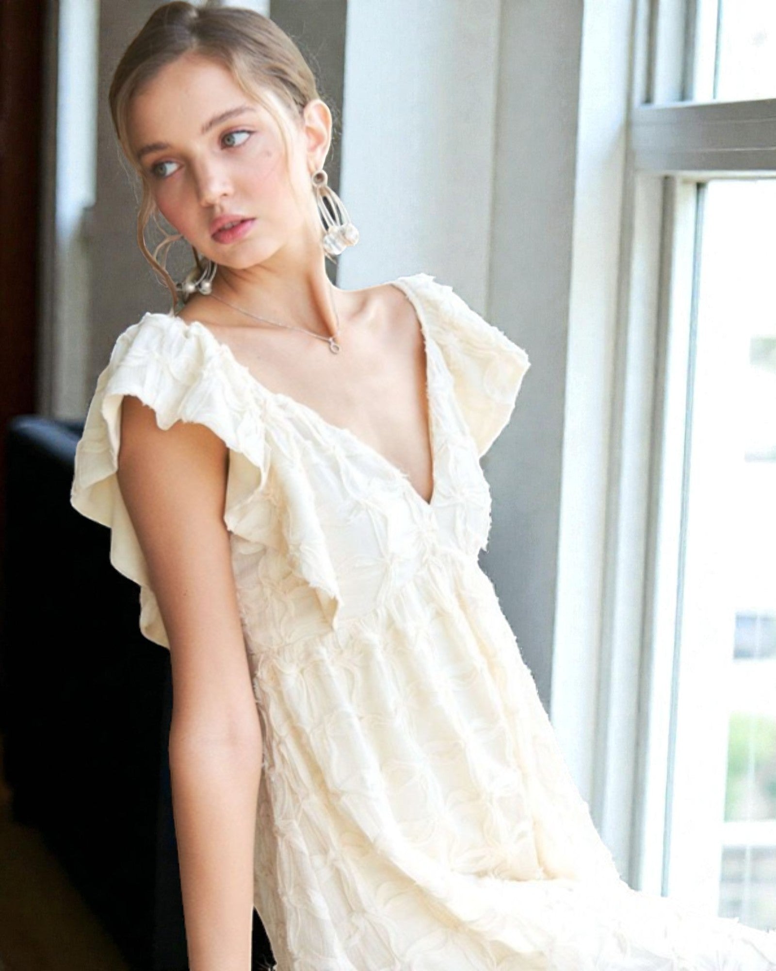 Woman wearing a white off-shoulder dress in a room with large windows.