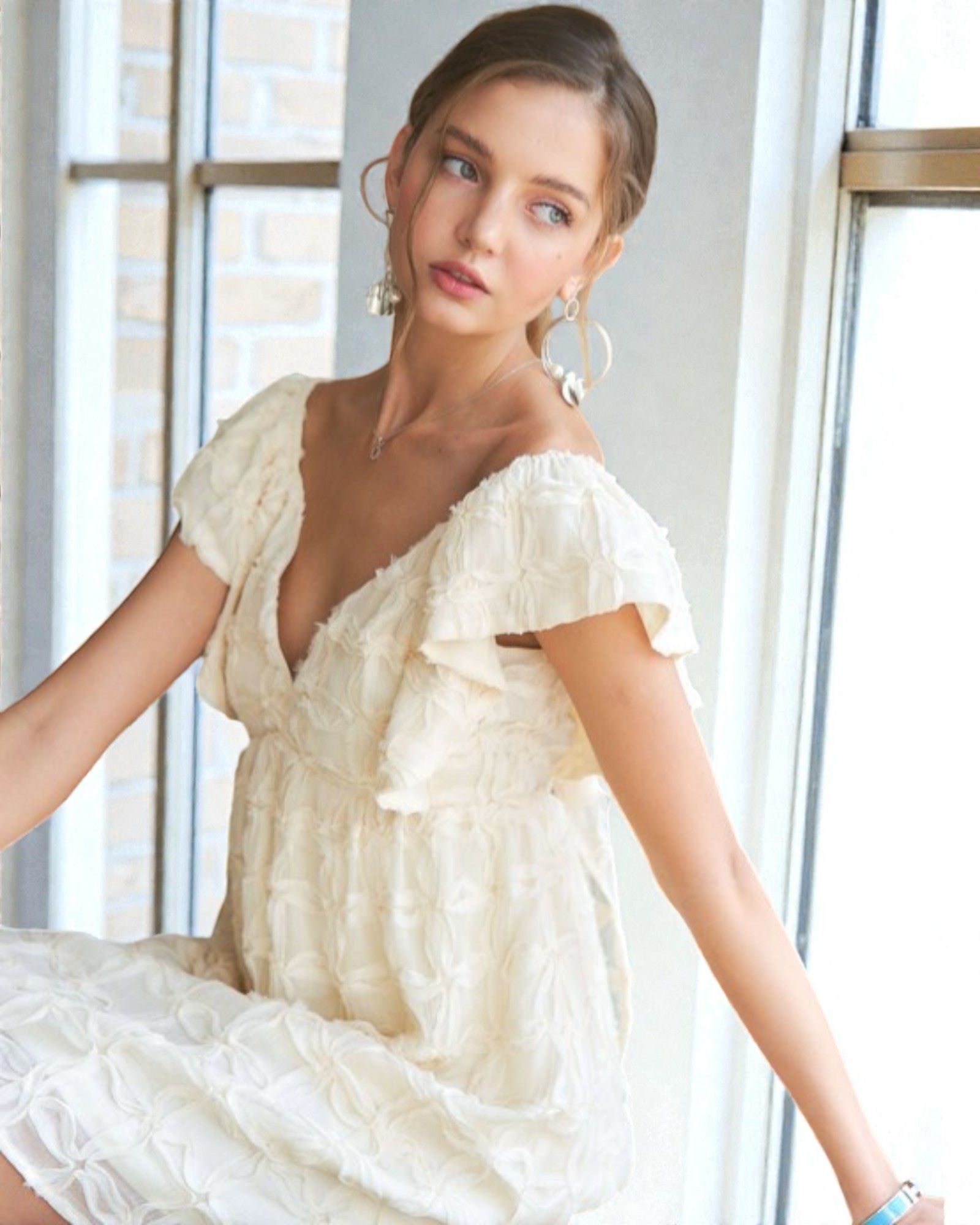 Woman wearing a white off-shoulder dress in a bright room.