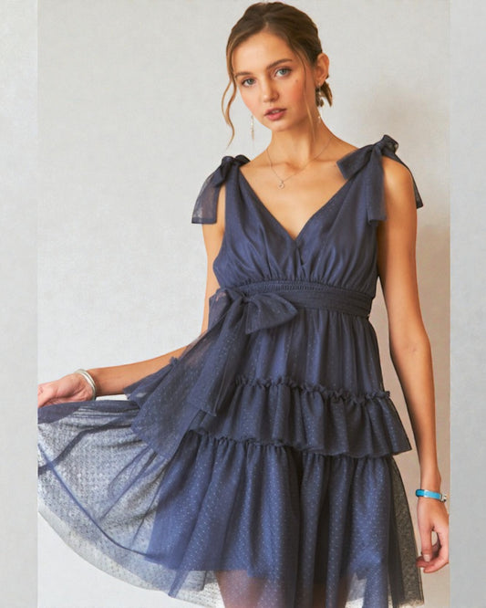 Woman wearing a navy blue dress with ruffled sleeves against a plain background