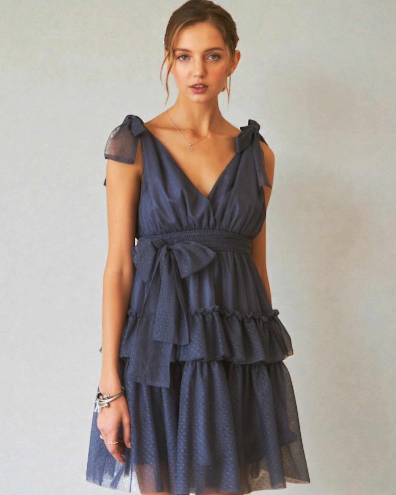 Woman wearing a navy blue dress with ruffled layers against a plain background