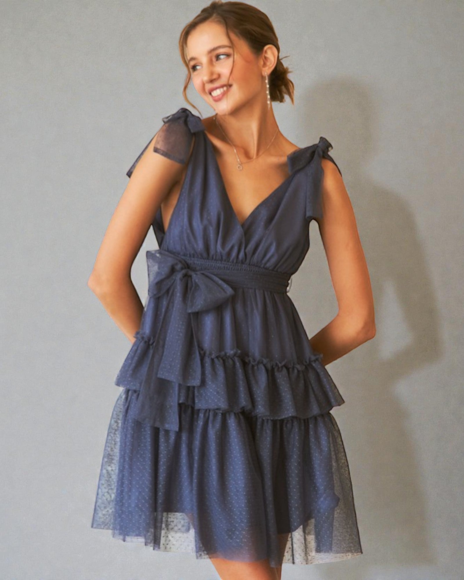 Woman wearing a navy blue dress with ruffled layers against a plain background