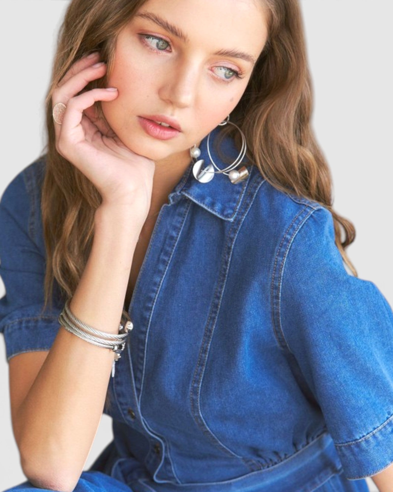 Woman wearing a blue denim dress with hoop earrings against a plain background