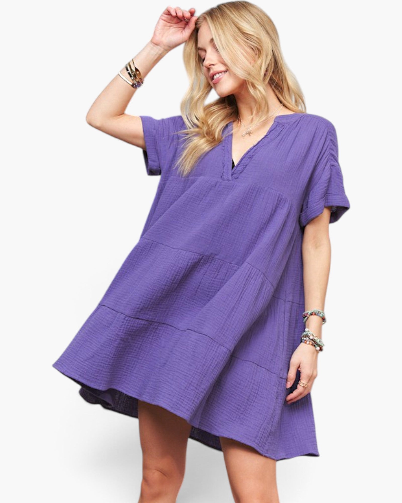 A woman wearing a loose, short-sleeve purple dress with a V-neck and gathered tiered skirt, posed against a clean white studio background.