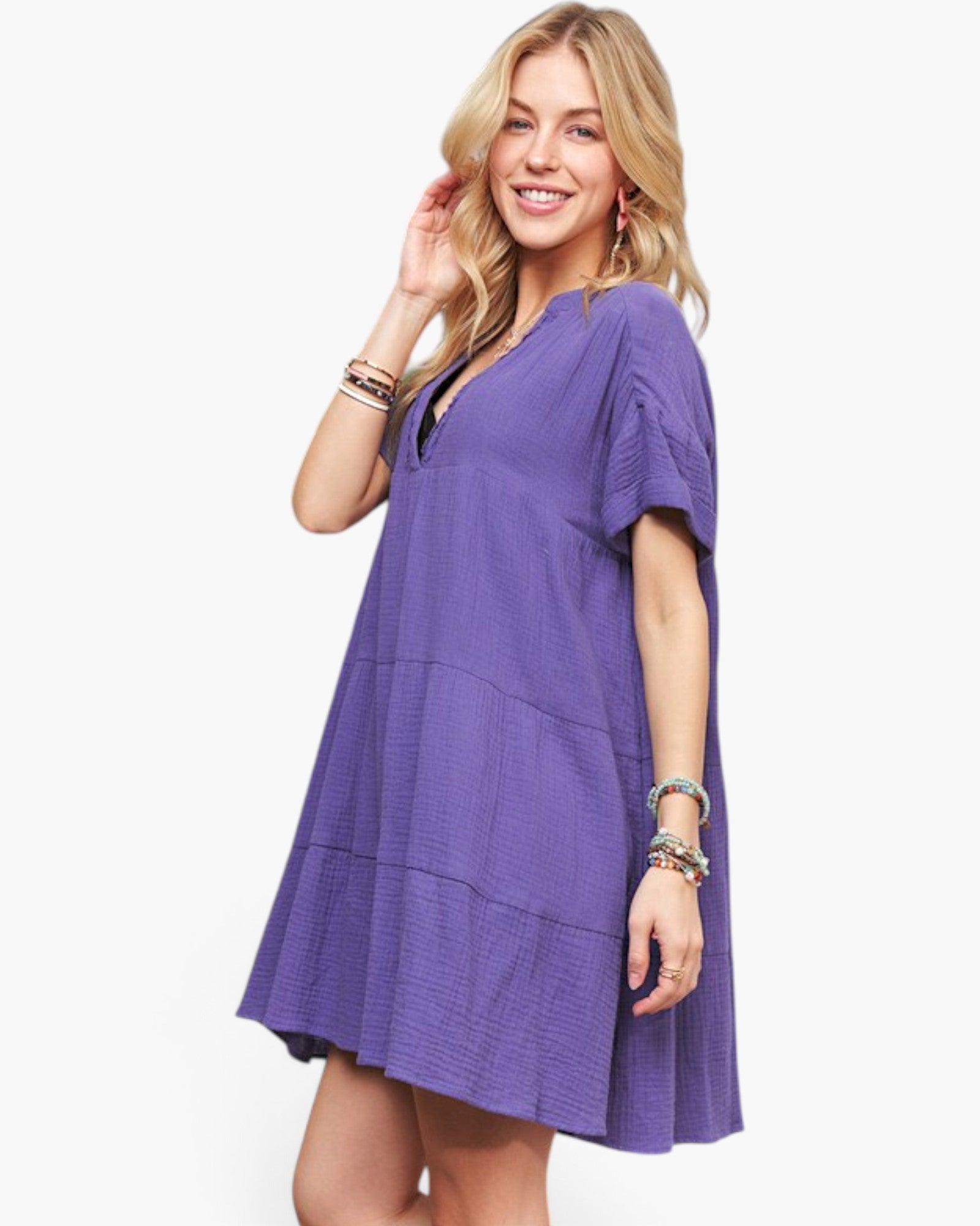 A woman modeling a purple short-sleeve tiered mini dress with a V-neckline, photographed against a clean white studio background.