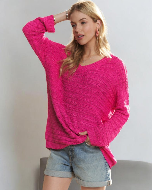 Woman wearing a bright pink sweater and denim shorts against a plain background