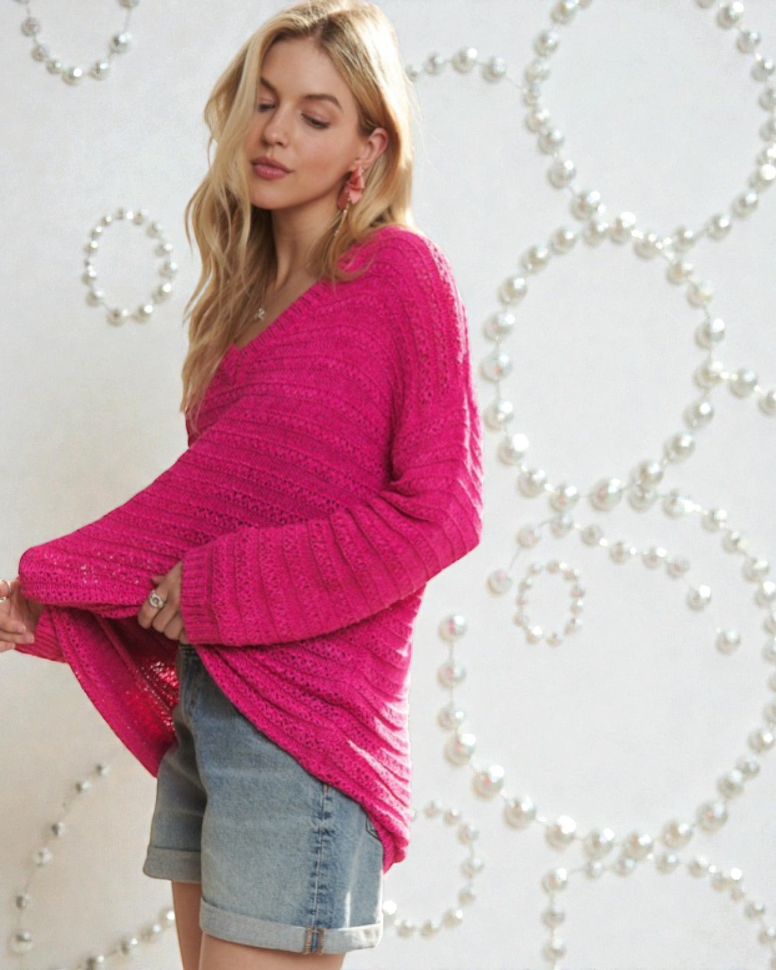 Woman wearing a bright pink sweater and denim shorts against a decorative white background