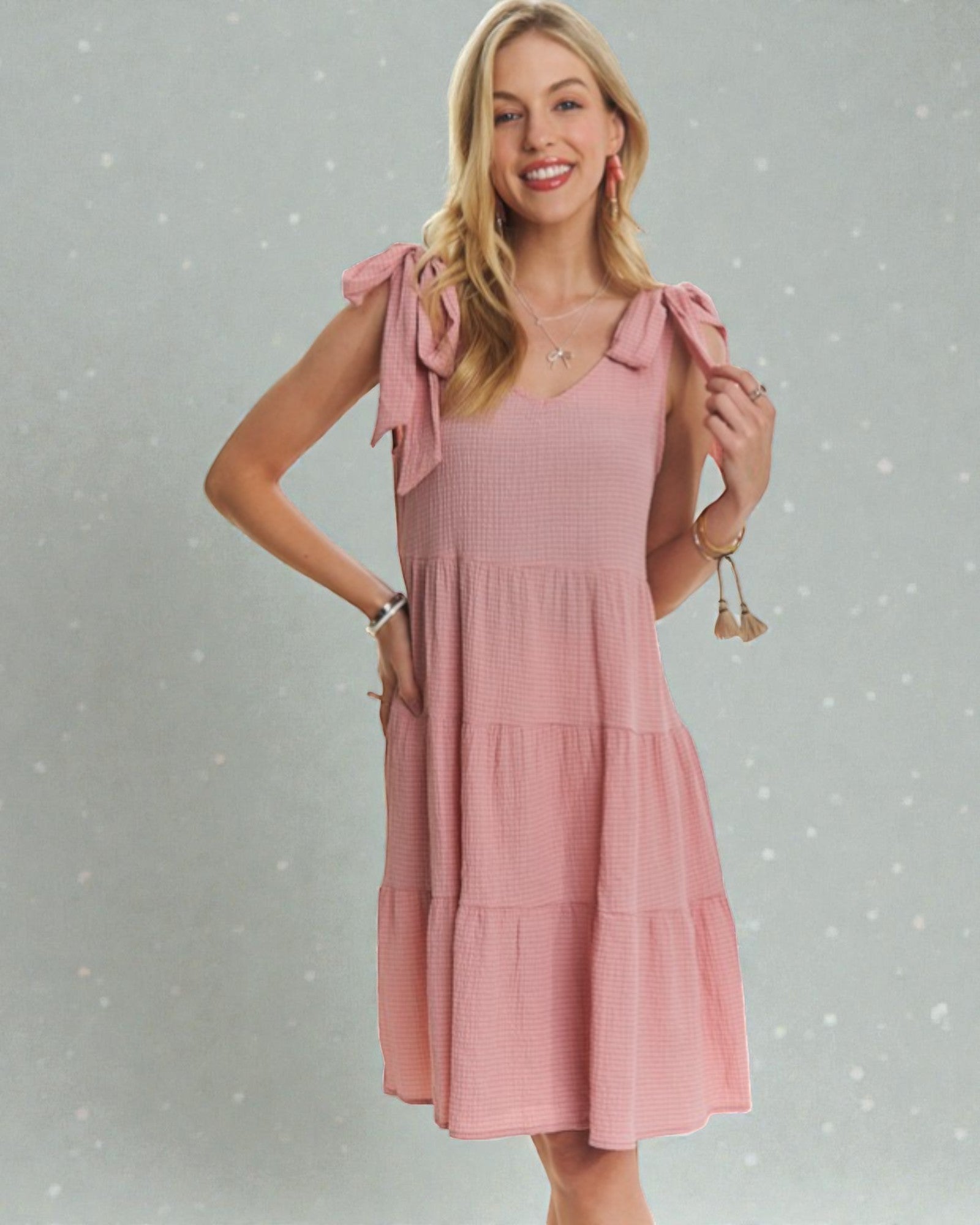 Woman wearing a pink dress with bow sleeves against a gray background