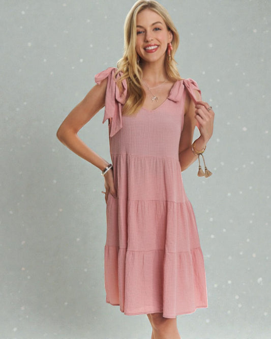 Woman wearing a pink dress with bow sleeves against a gray background