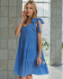 Woman wearing a blue dress with a tie shoulder detail indoors.