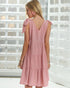 Woman wearing a pink dress with bow straps against a white brick wall.