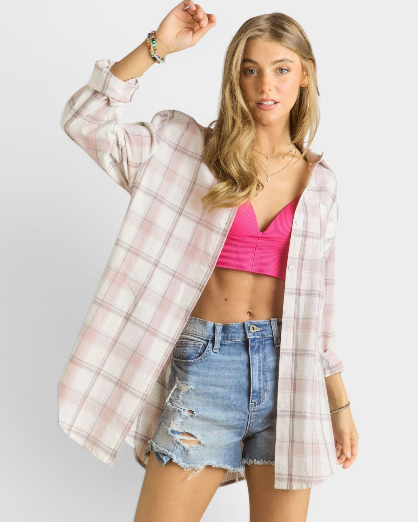 Woman wearing a plaid shirt over a pink crop top and denim shorts on a white background