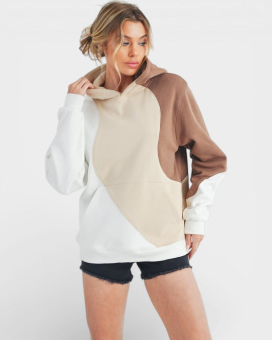 Woman wearing a color-blocked hoodie with white, beige, and brown sections on a white background.