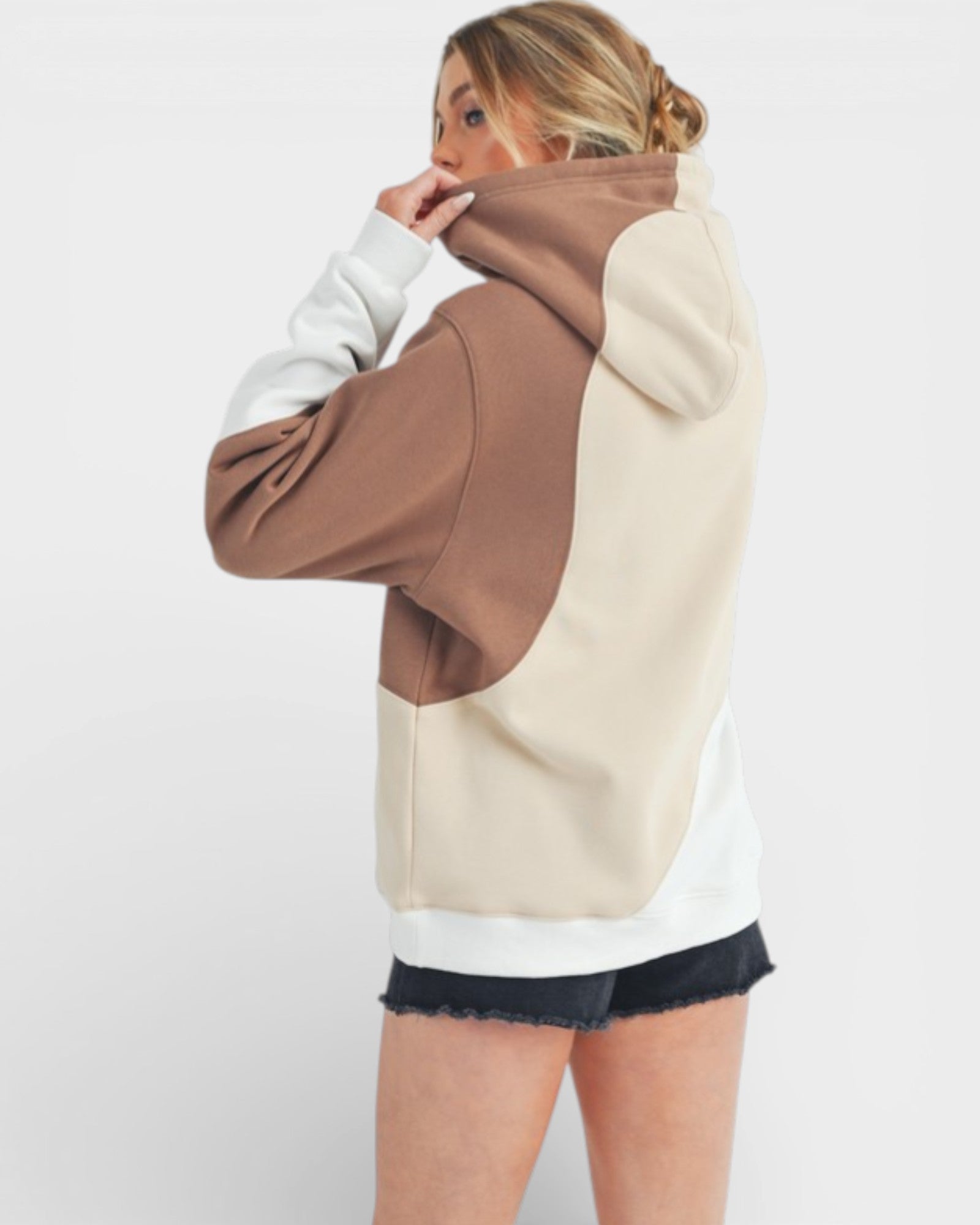 Person wearing a color-blocked hoodie with brown, beige, and white sections on a plain background