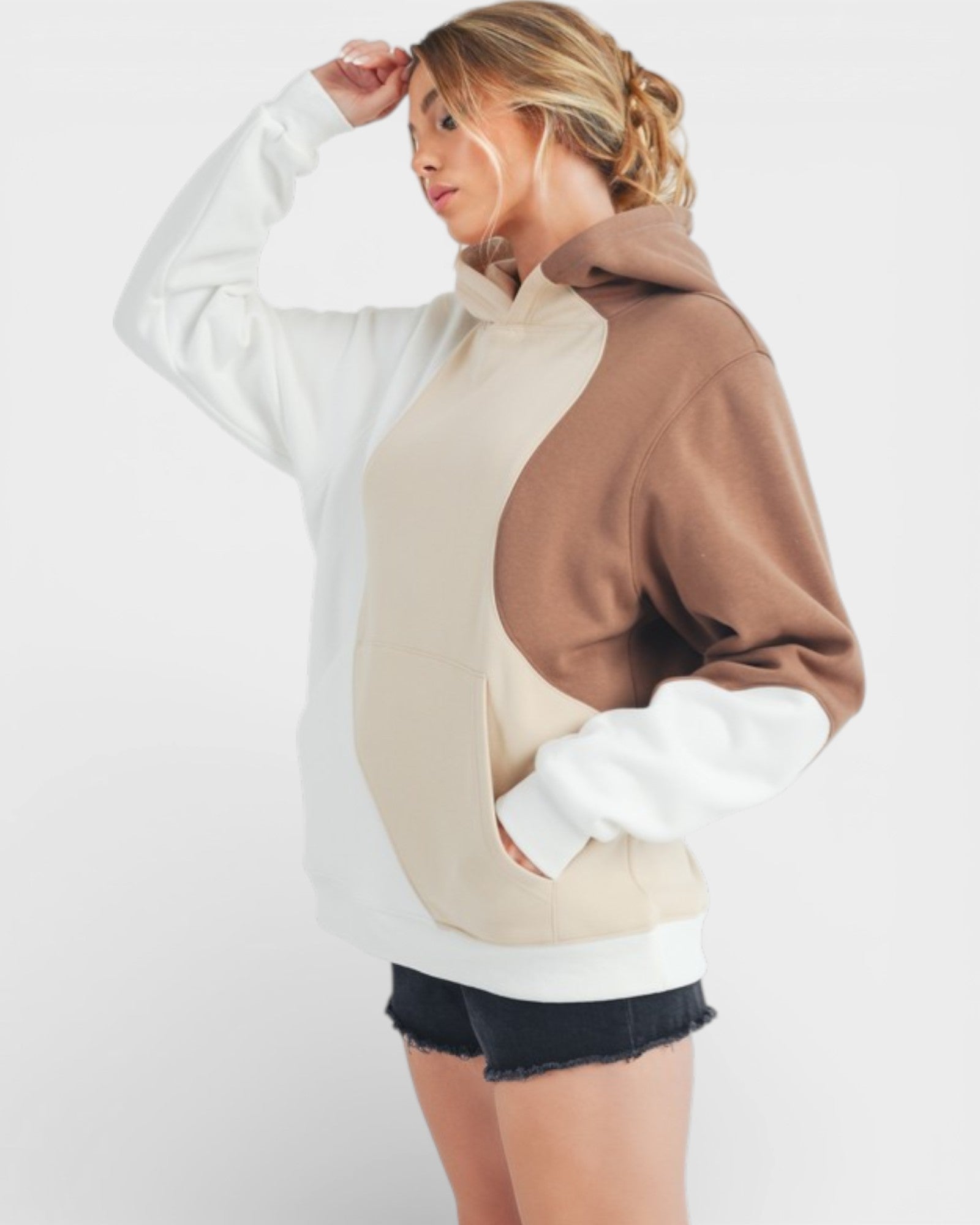 Person wearing a color-blocked hoodie with white, beige, and brown sections on a plain background.
