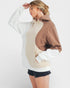 Person wearing a color-blocked hoodie with white, beige, and brown sections on a plain background.