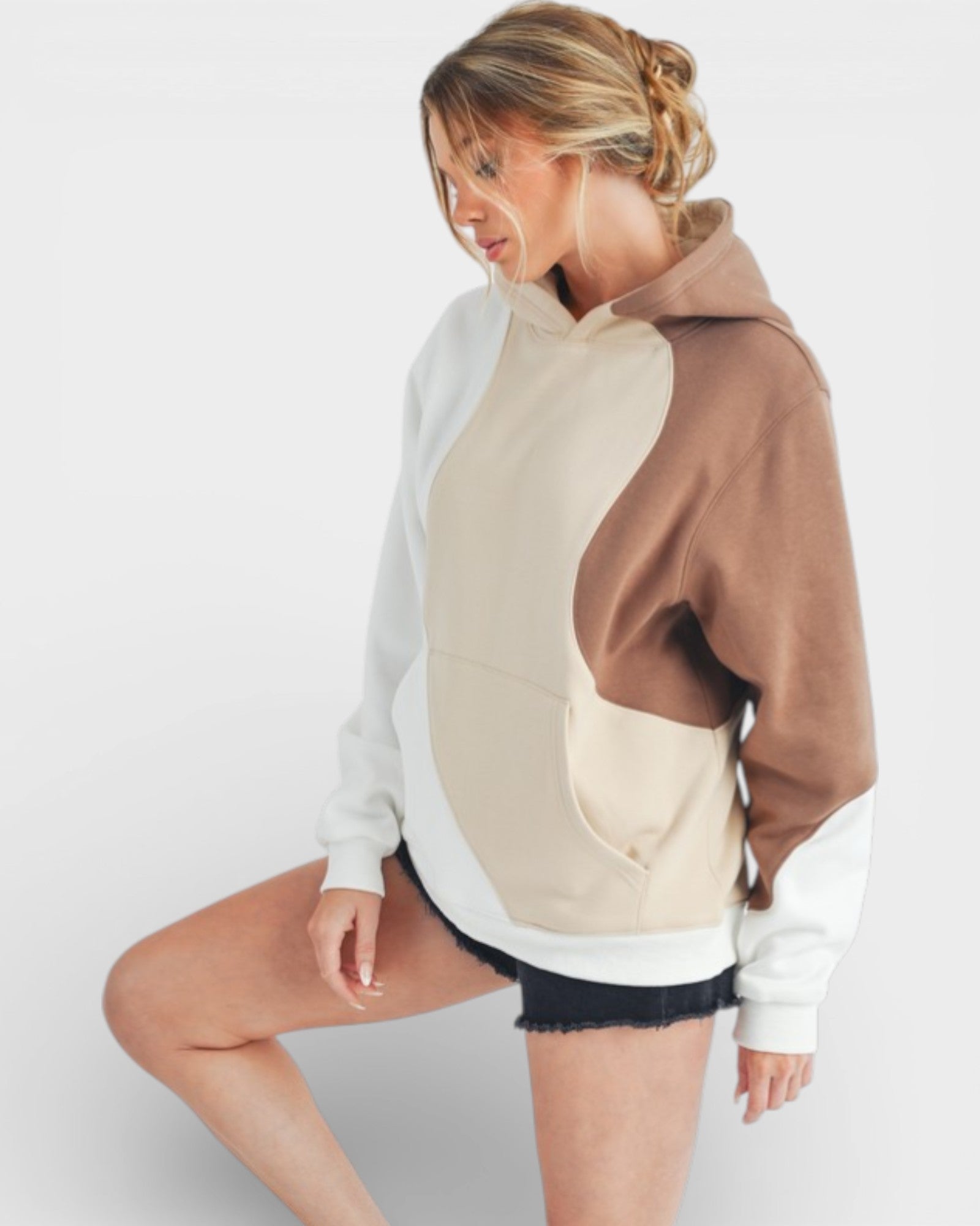 Woman wearing a color-blocked hoodie with white, beige, and brown sections on a plain background.