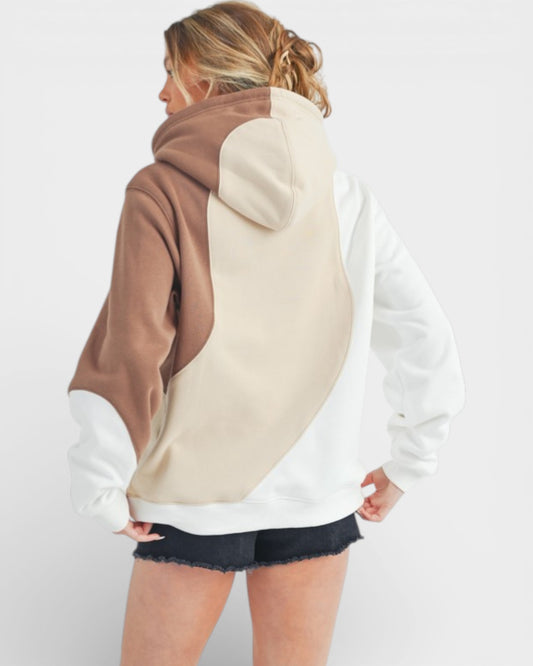 Woman wearing a color-blocked hoodie with brown, beige, and white sections on a plain background.