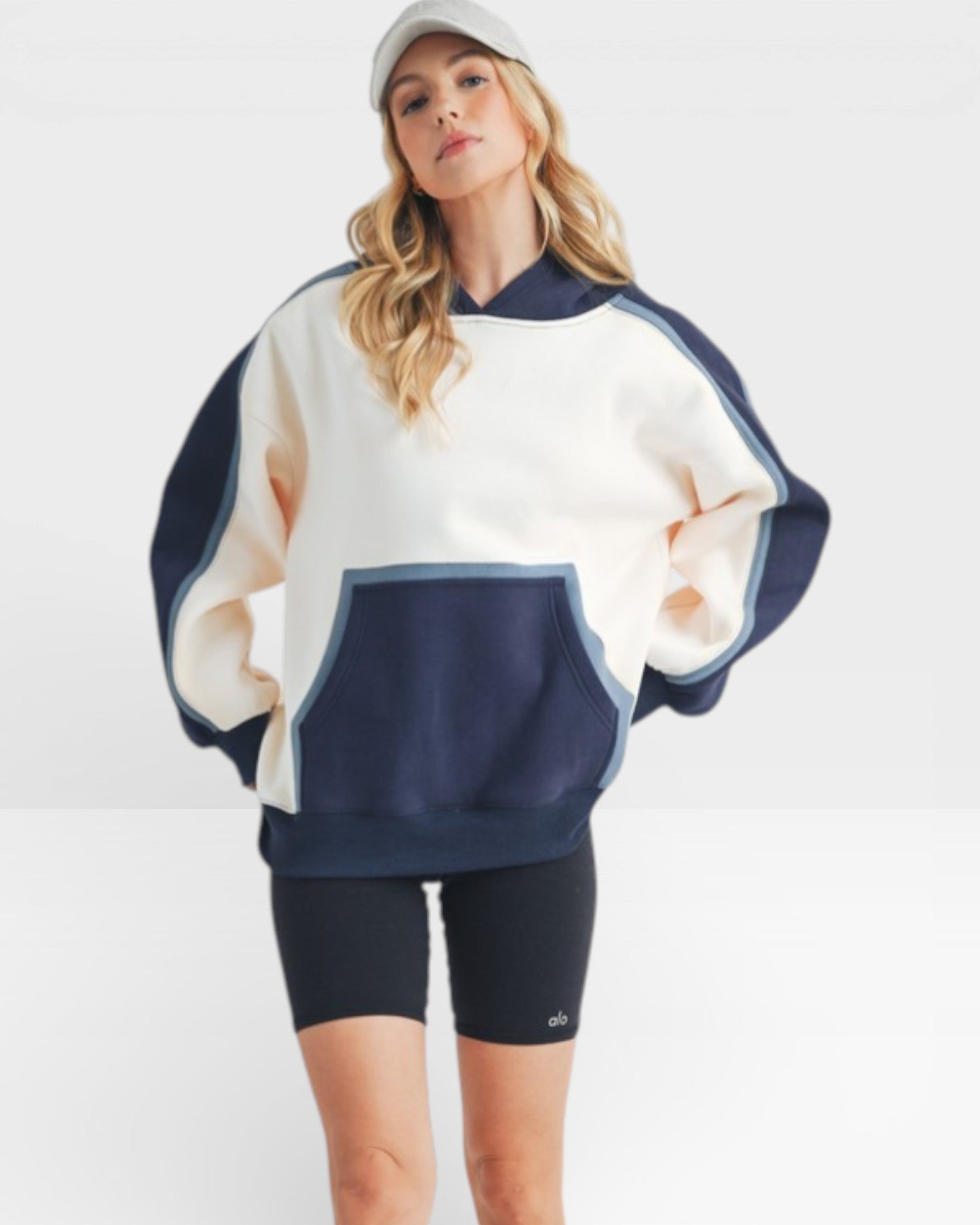 Woman wearing a white and navy oversized sweater with black shorts on a white background
