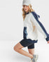 Woman wearing a white and navy tracksuit with black shorts on a white background