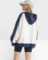 Woman wearing a white and navy blue hooded jacket on a plain background