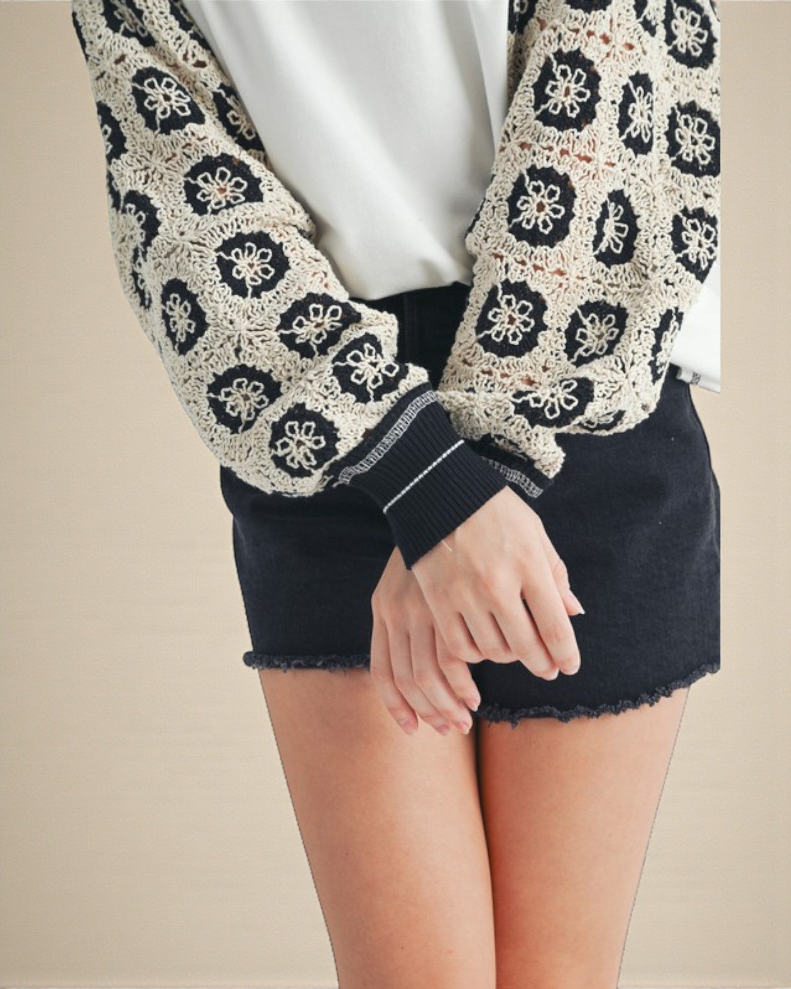 Person wearing a patterned cardigan over a white shirt with a black skirt.