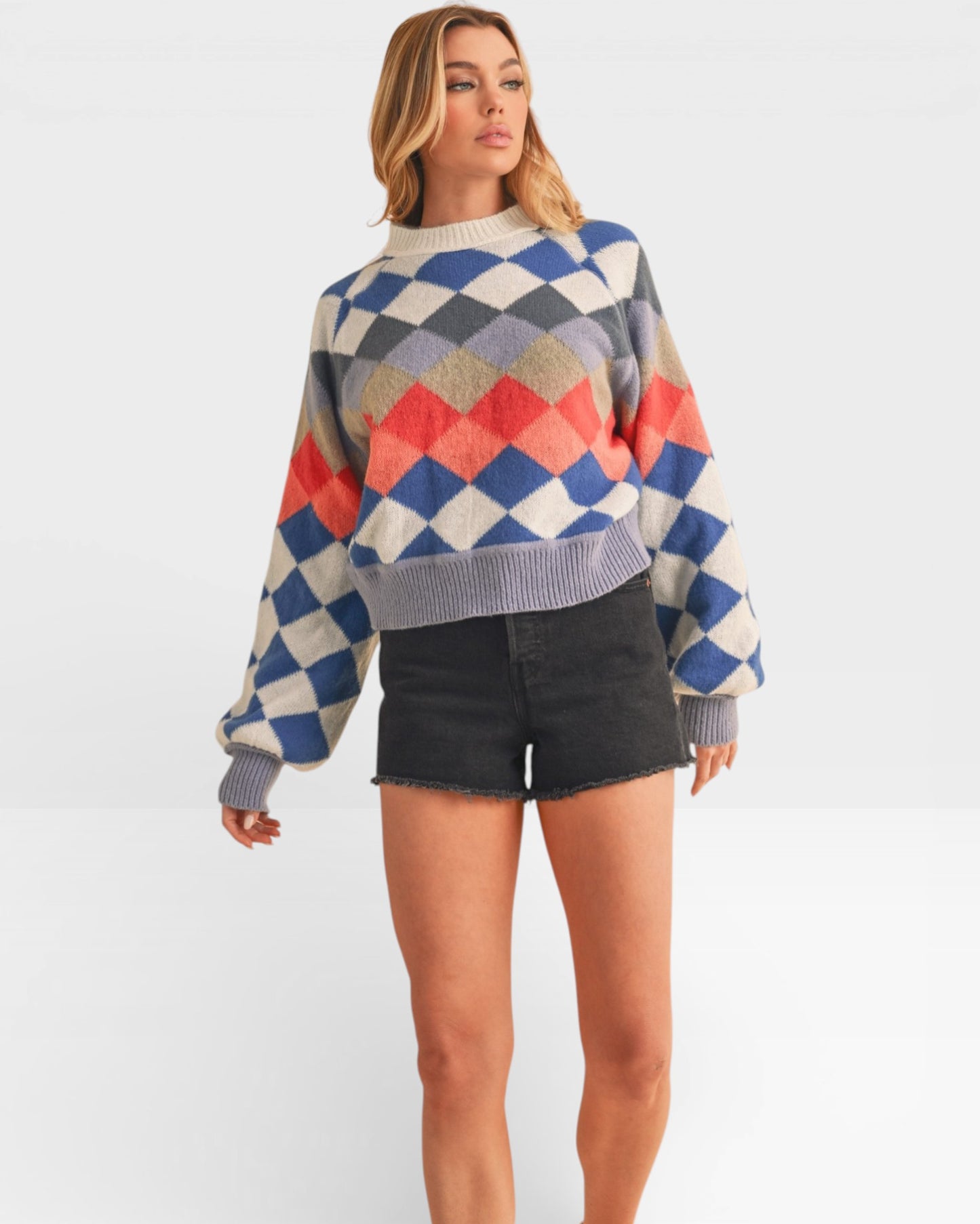 Woman wearing a colorful diamond pattern sweater and black shorts on a white background