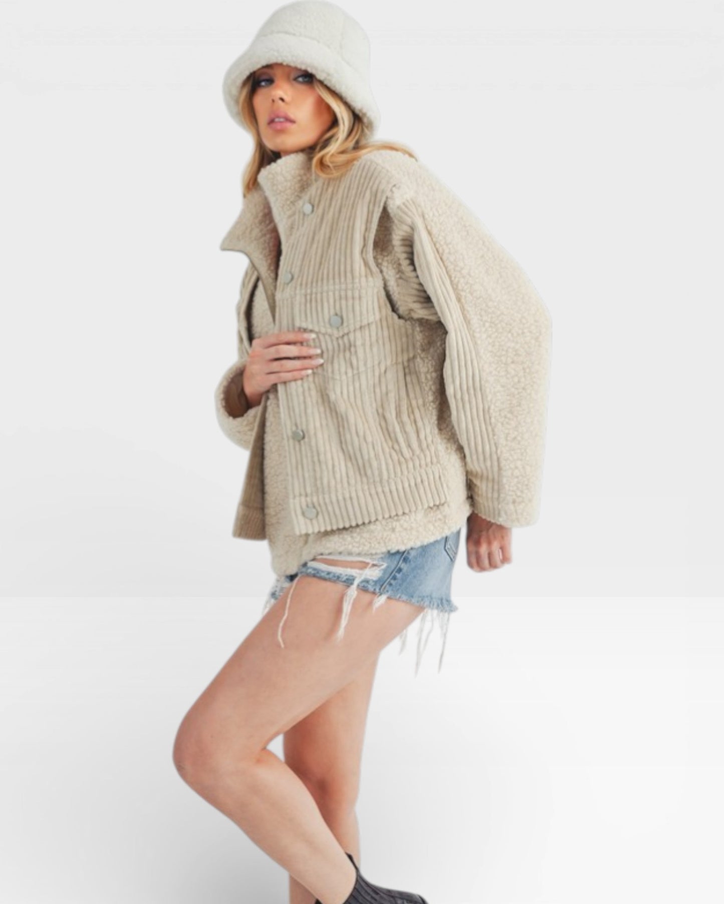 Woman wearing a beige knit sweater and vest with denim shorts on a white background