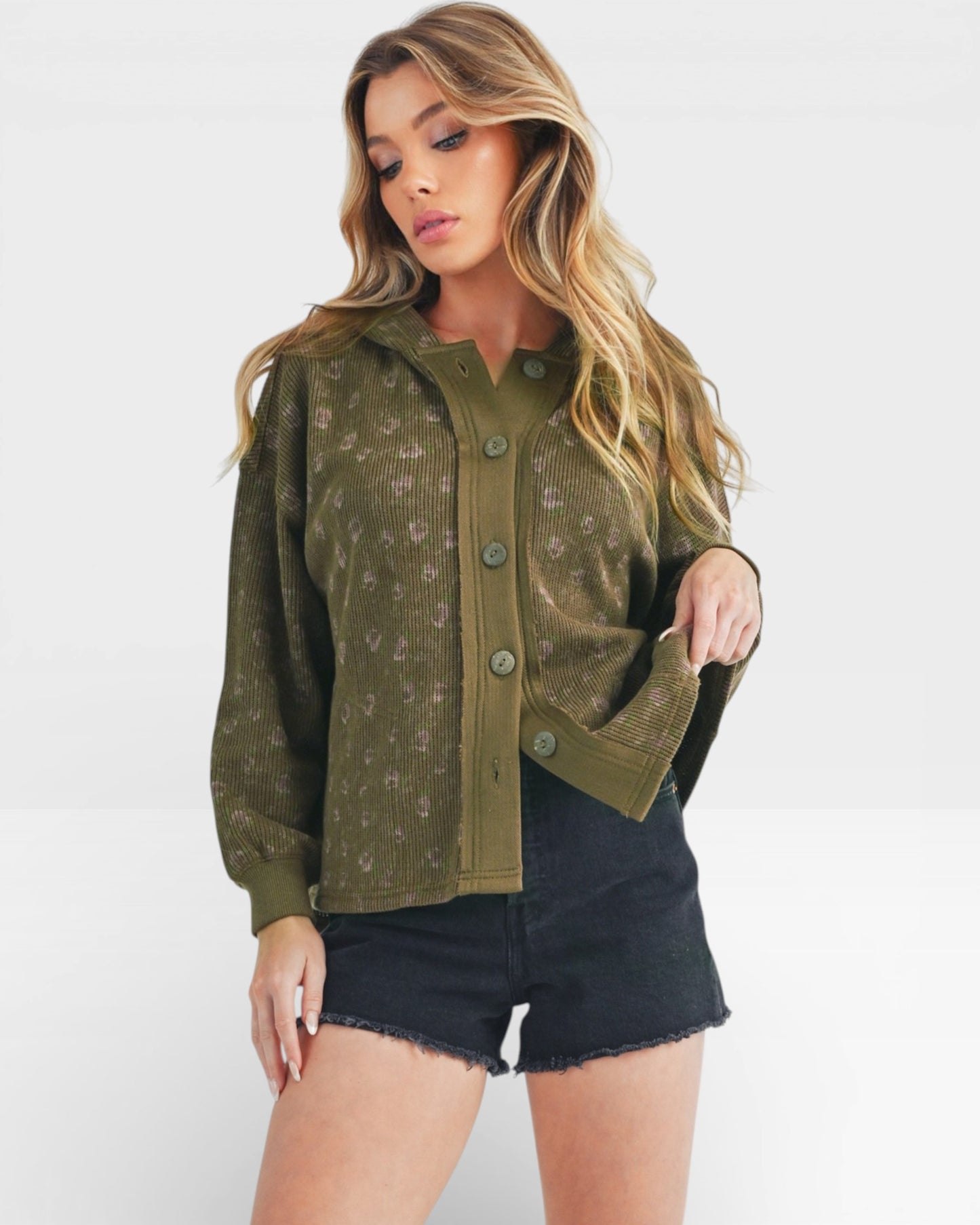 Woman wearing an olive green cardigan over a black top and shorts on a white background