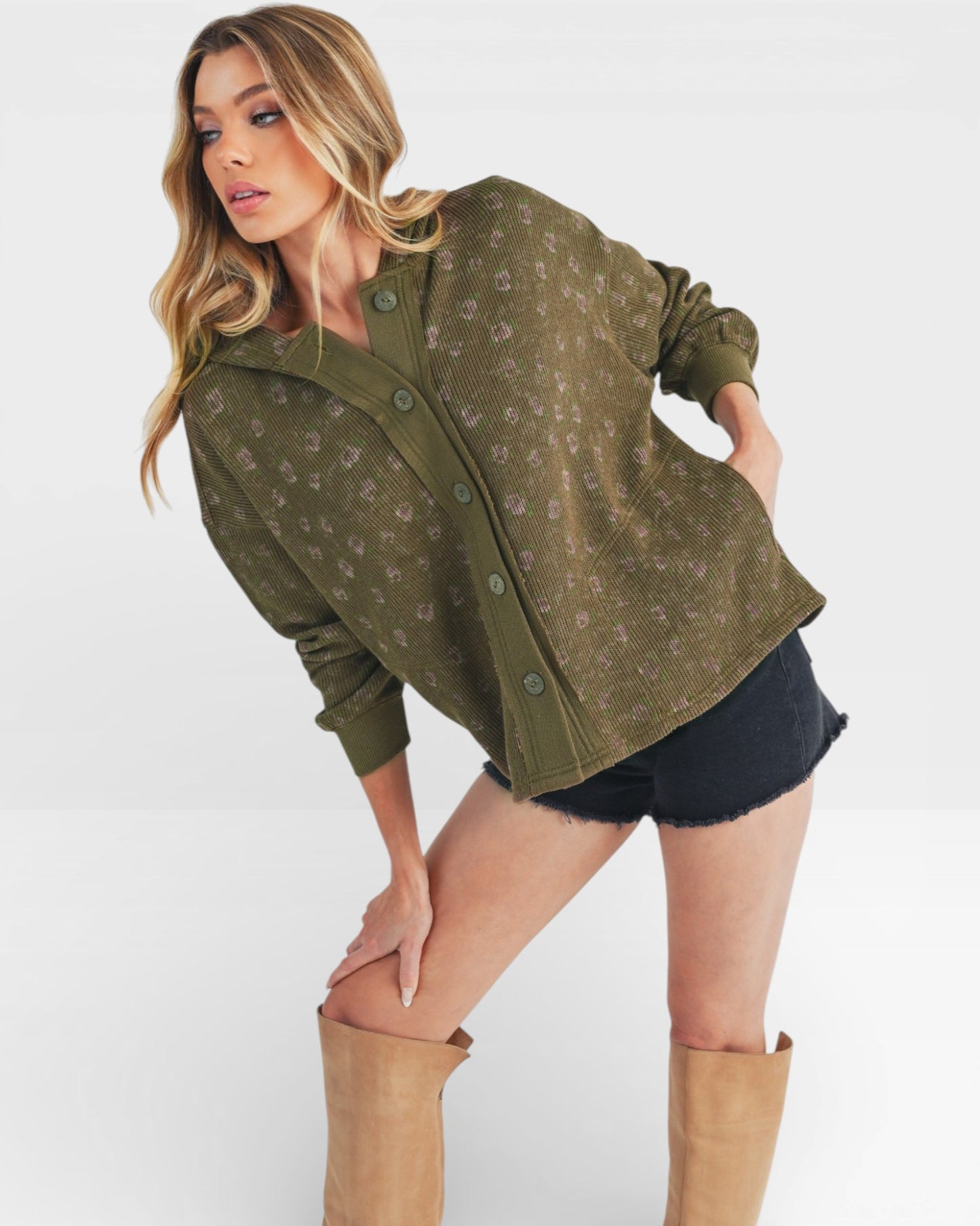 Woman wearing a green patterned jacket and black shorts with tan knee-high boots on a white background