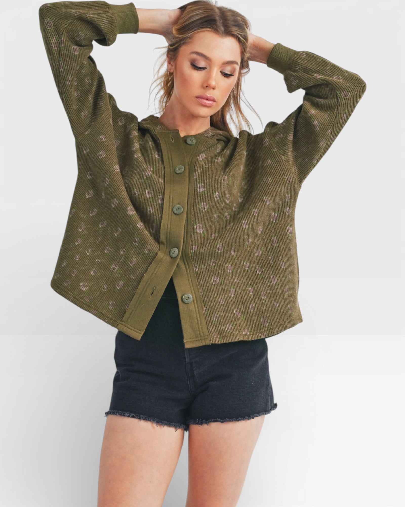 Woman wearing a green patterned cardigan over black shorts on a white background
