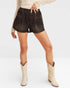 Person wearing dark denim shorts and white cowboy boots on a plain background