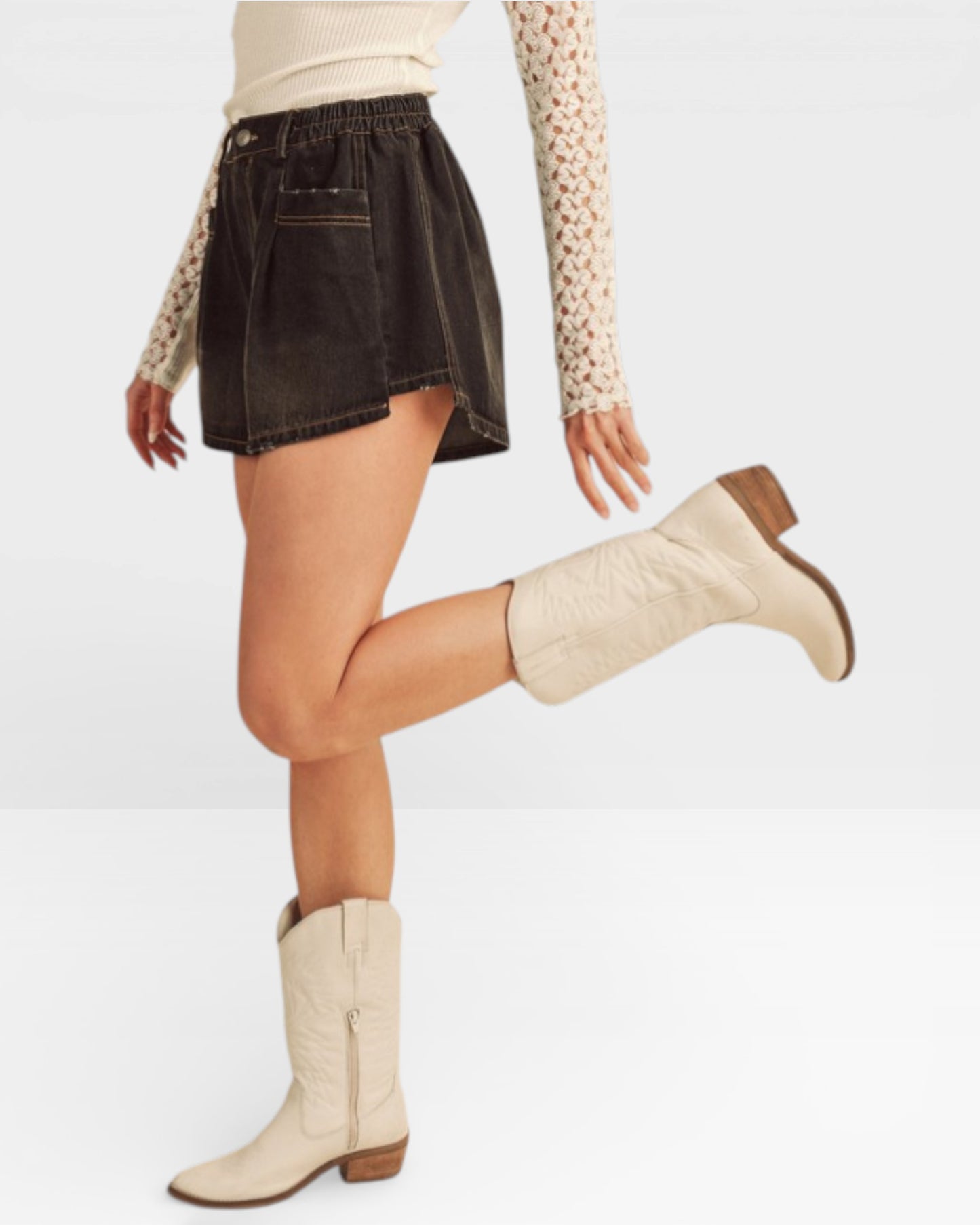 Person wearing a black denim skirt and beige knee-high boots on a white background