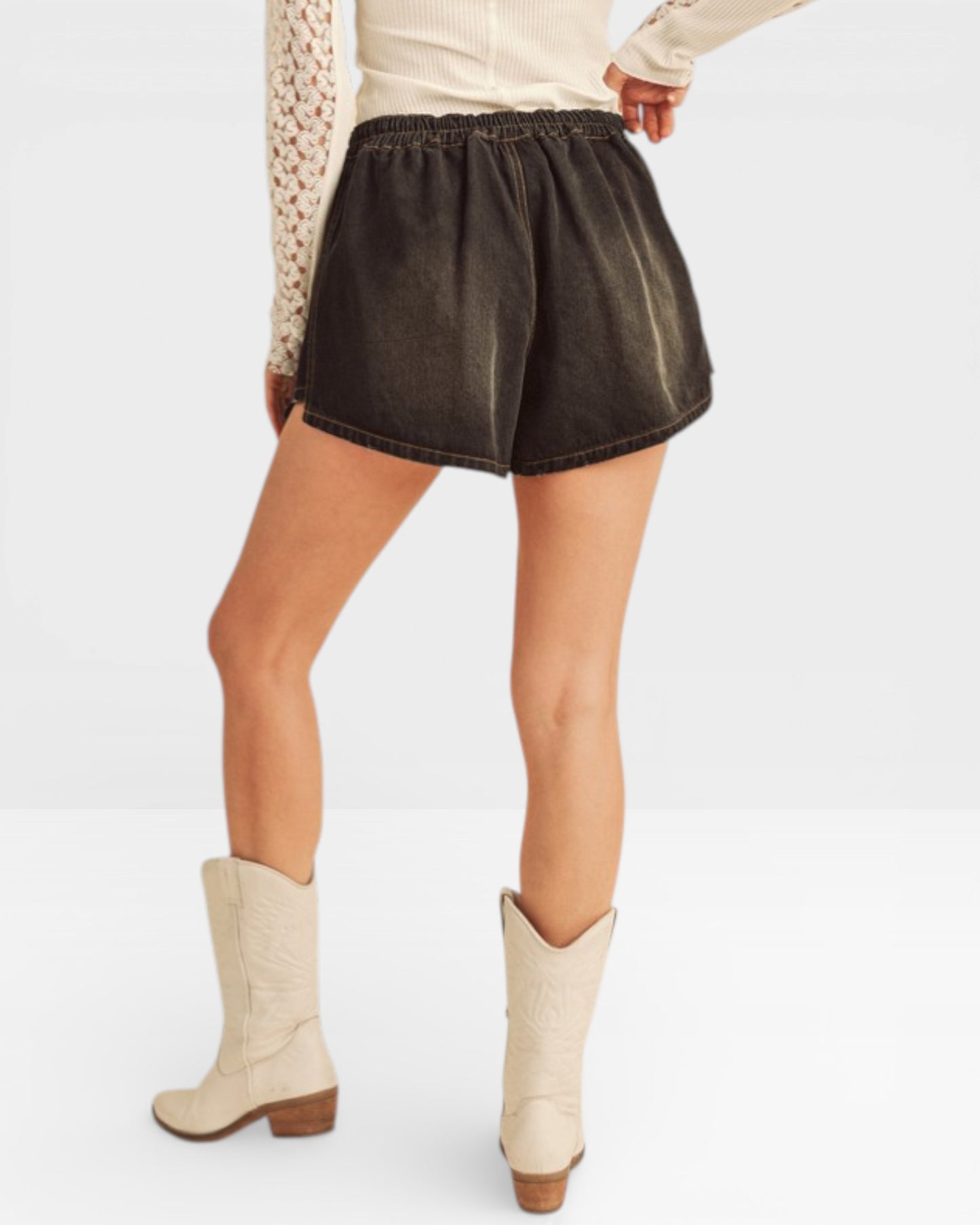 Person wearing dark denim shorts and white boots on a light gray background