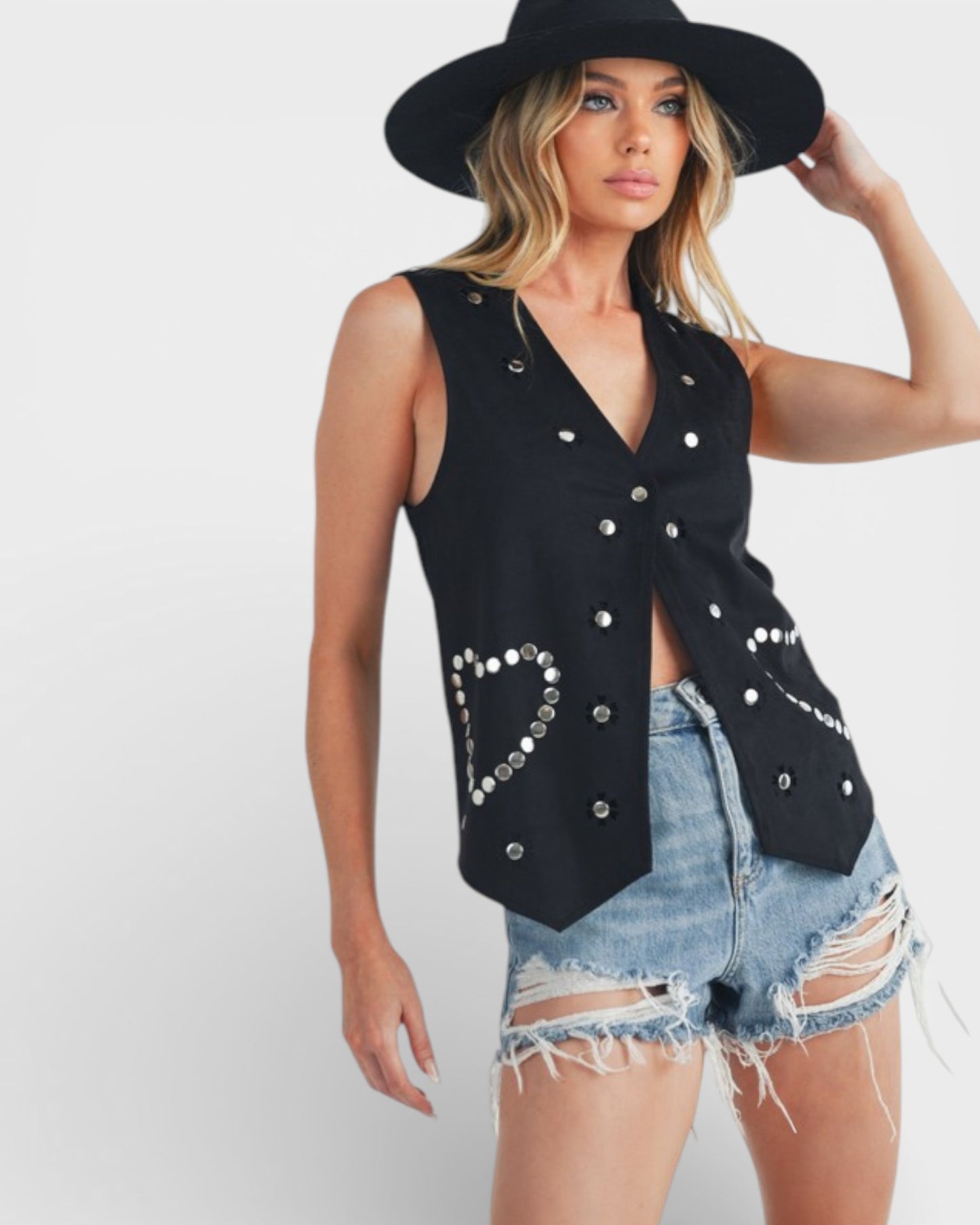 Woman wearing a black sleeveless top with silver buttons and denim shorts on a white background