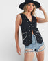 Woman wearing a black sleeveless top with silver buttons and denim shorts on a white background