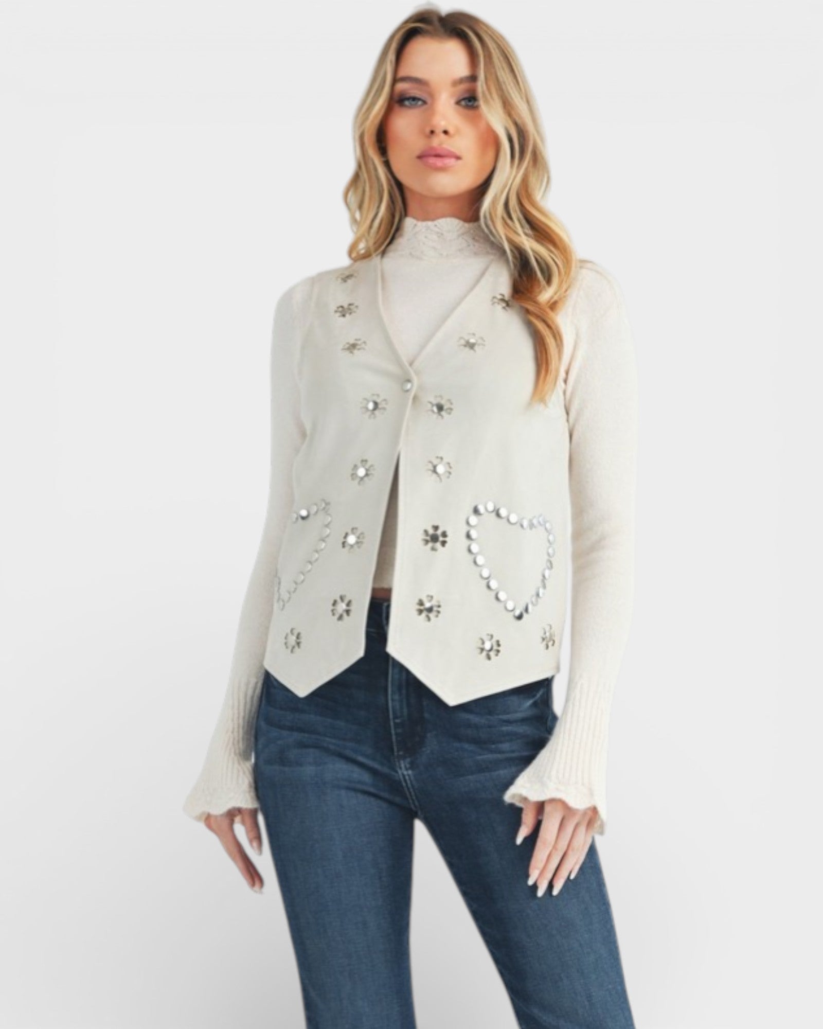Woman wearing a white embellished vest over a white blouse with blue jeans on a white background