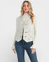 Woman wearing a white embellished vest over a white blouse with blue jeans on a white background