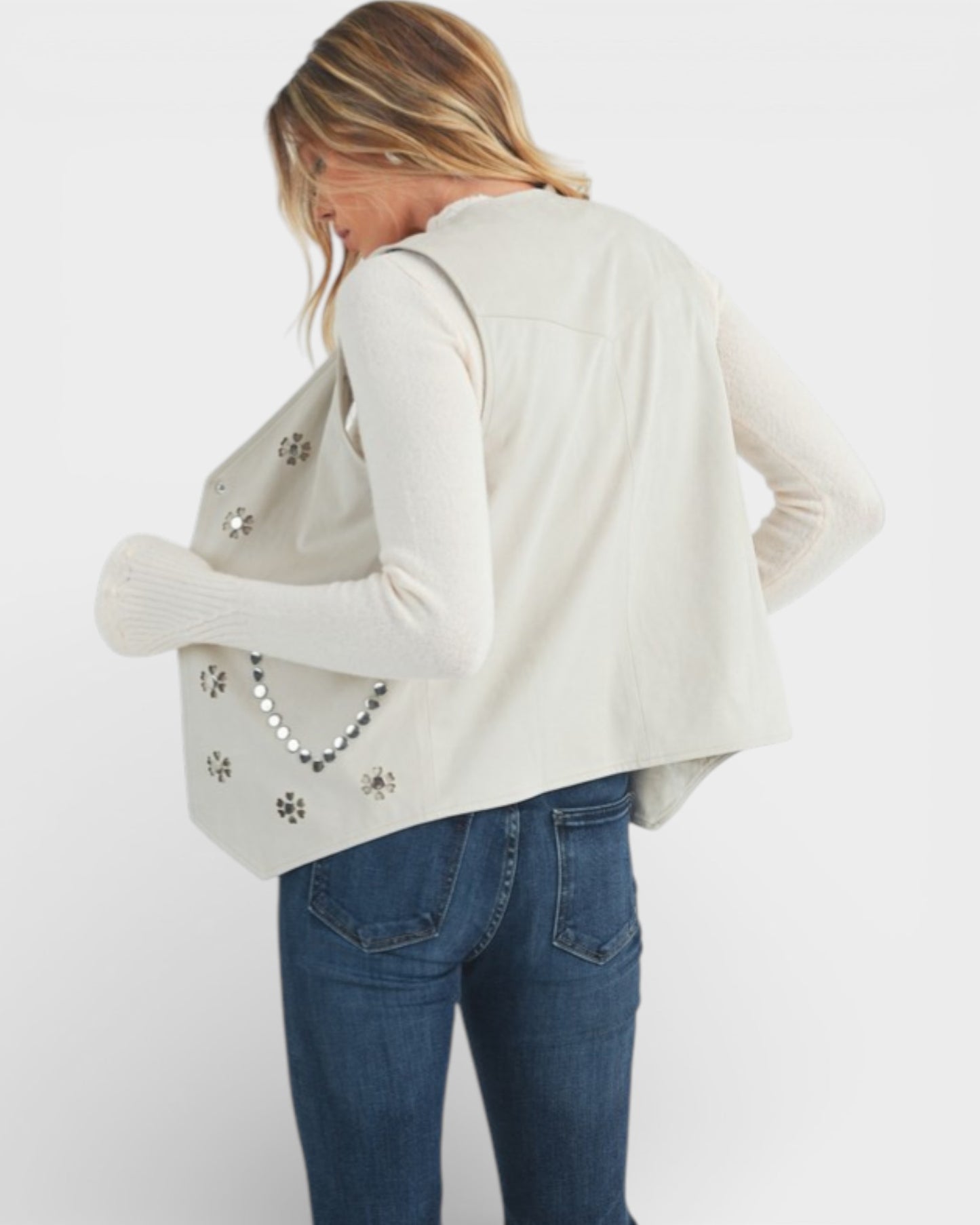 Woman wearing a beige cardigan and blue jeans with a white background