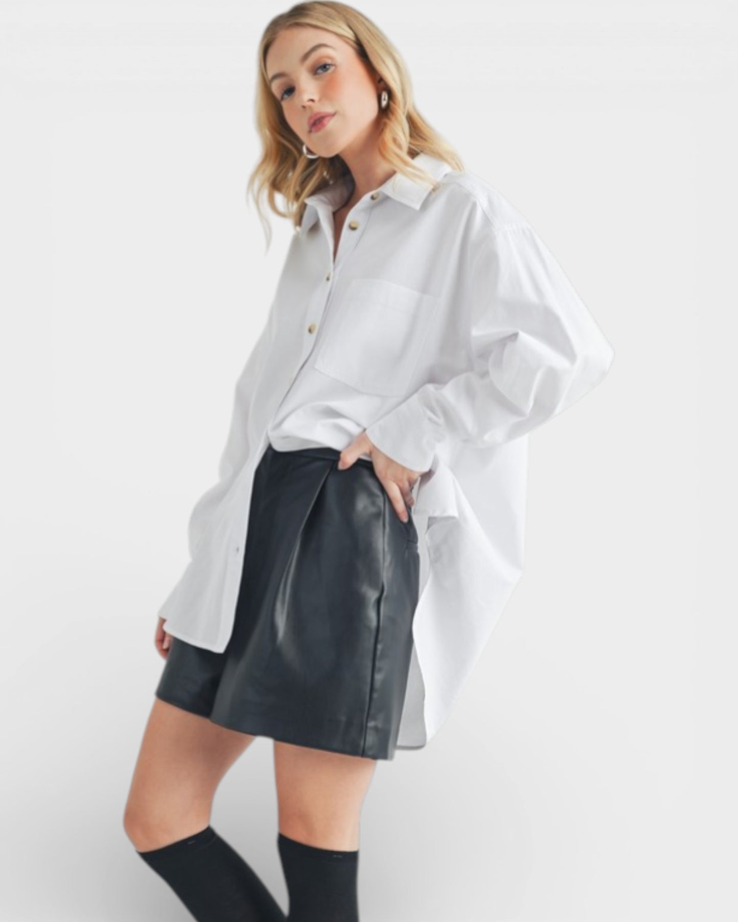 Woman wearing a white oversized shirt and black leather skirt on a white background